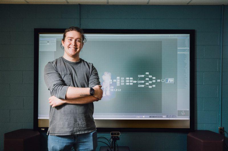 Josh Taibbi stands in front of a screen displaying programming for the interactive light wall exhibit he developed.